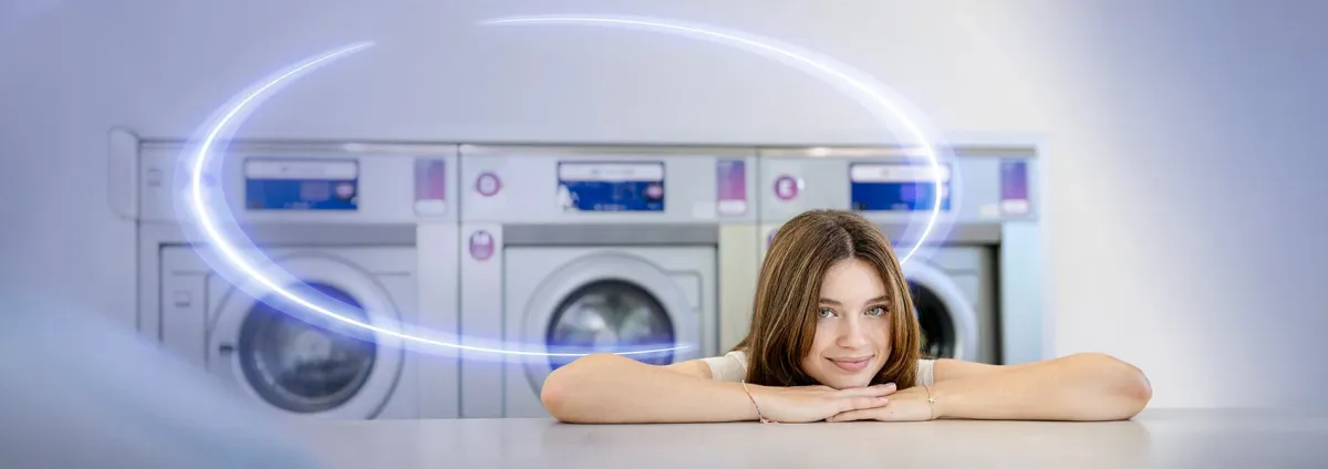 Smiling woman resting on a counter in front of a row of commercial washing machines
